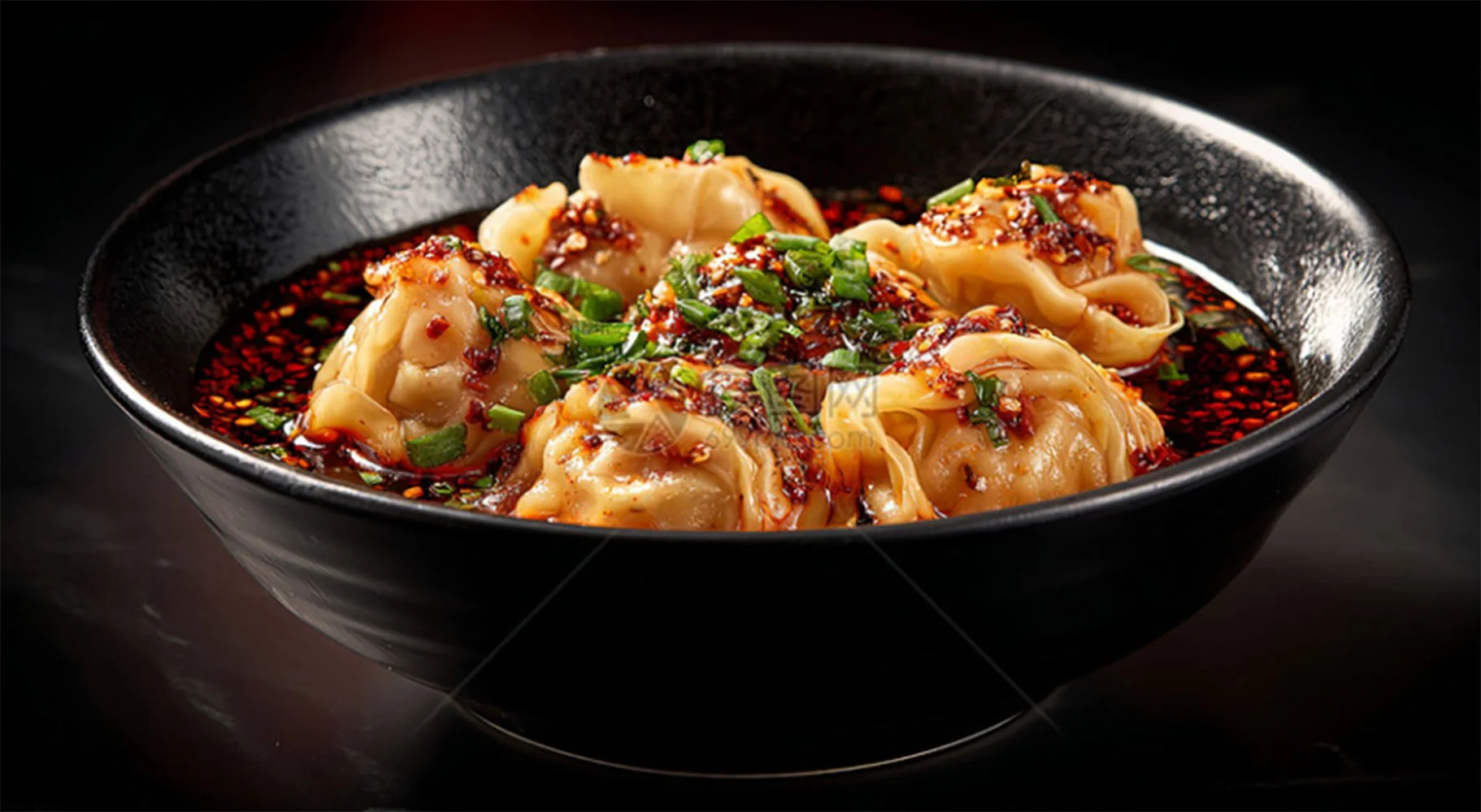 Haufen von chinesischen Teigtaschen in einer schwarzen Schüssel mit roter Sojasauce und grünen Frühlingszwiebeln