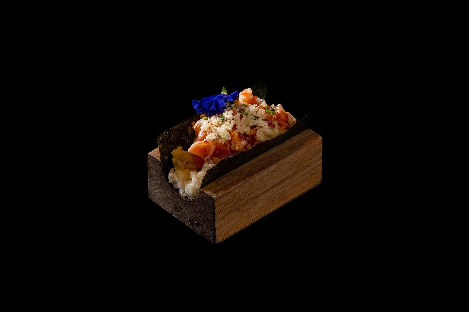 Sushi in Holzschale mit rot-blauer Blume und schwarzen Nori-Algen