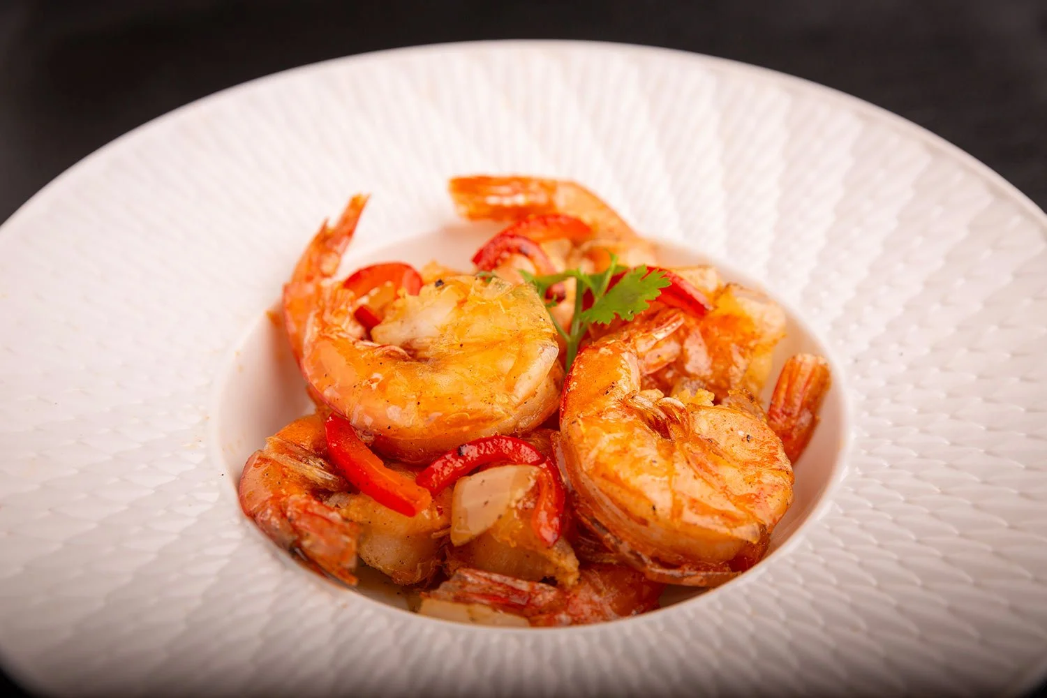 Gedünstete Garnelen mit roten Paprikastreifen auf einem weißen Teller mit dekorativem Muster.