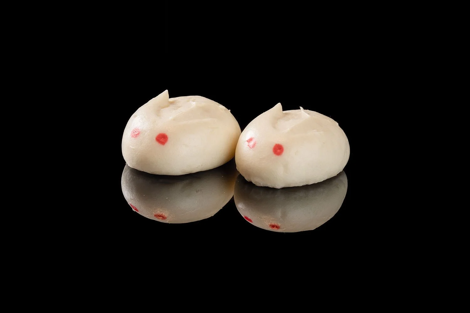 Zwei weiße Maki-Kuchen mit rotem Punkt, spiegelnd auf einer schwarzen Oberfläche.