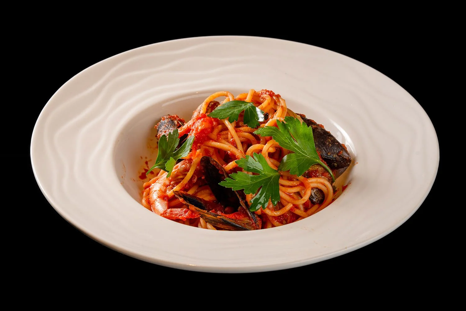 Pasta mit Meeresfrüchten und frischer Petersilie auf weißem Teller gegen schwarzen Hintergrund.