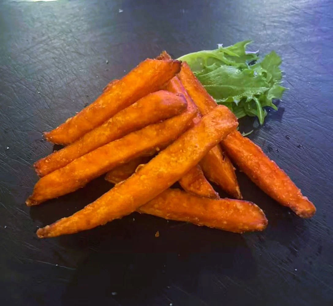 Süße Kartoffel-Pommes auf schwarzem Teller mit Salatblättern