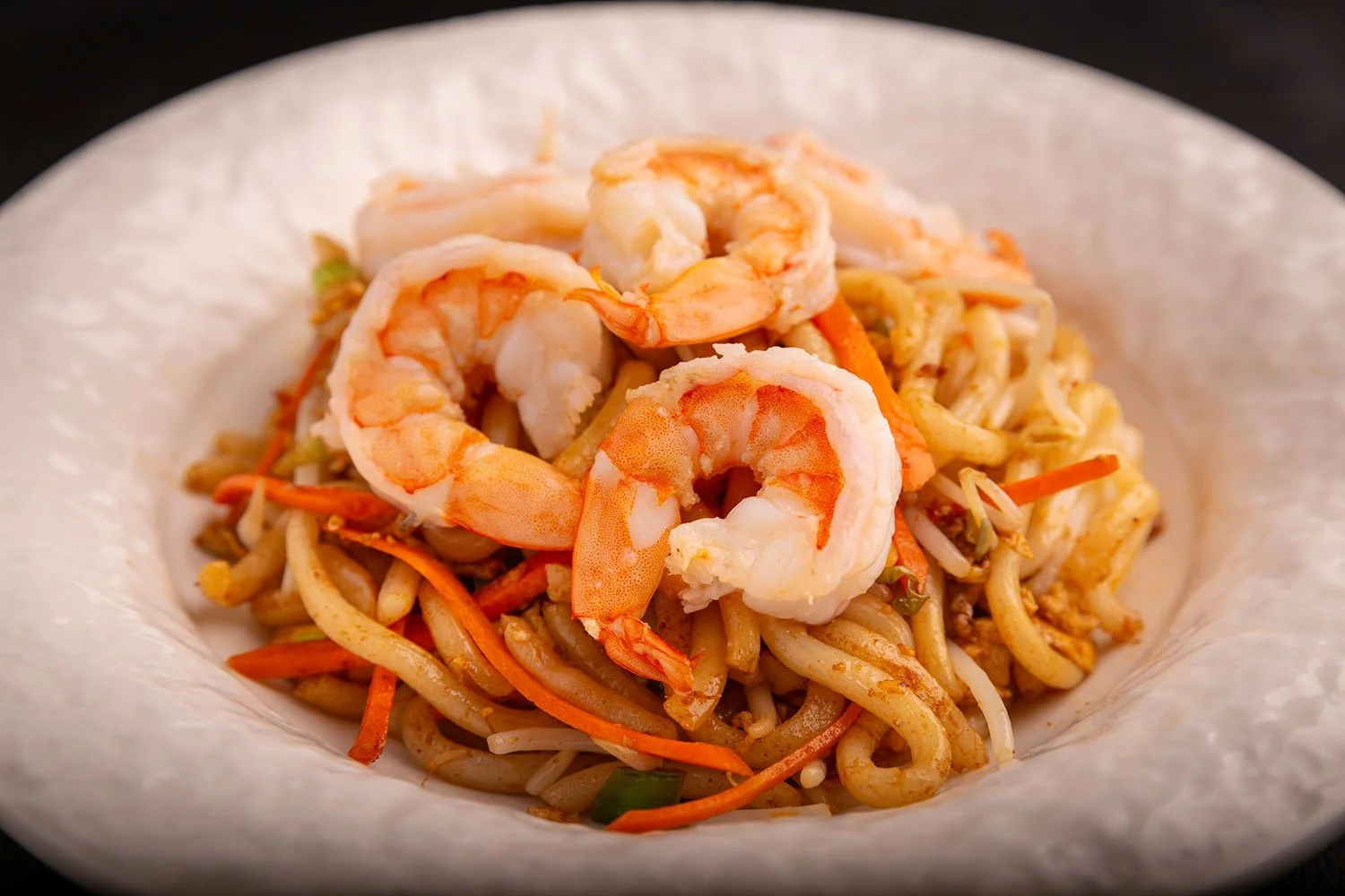 Gebratene Nudeln mit Garnelen und Gemüse, serviert auf einem weißen Teller.