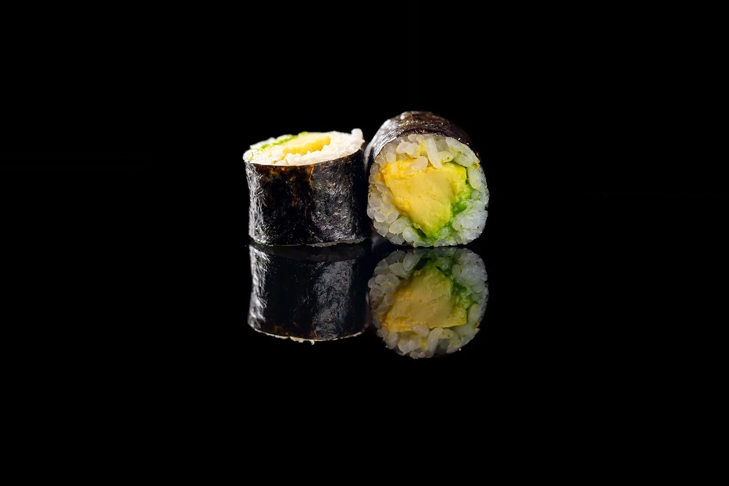 Zwei Sushi-Rollen mit Avocado und Ei, spiegelnd auf einer schwarzen Oberfläche