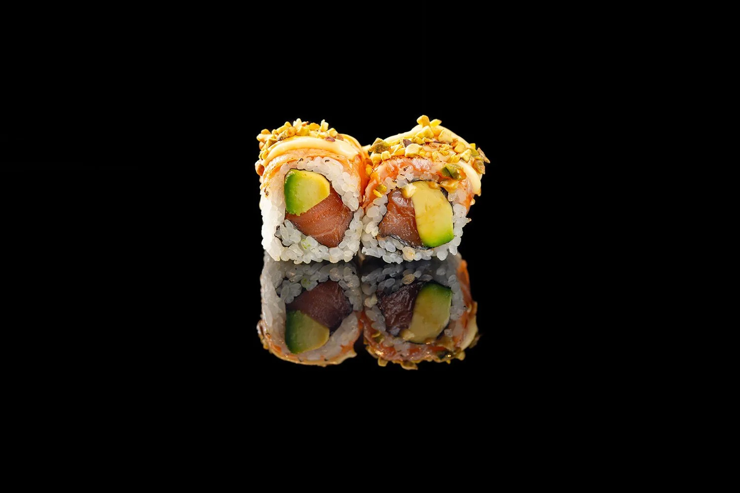 Nahaufnahme von zwei Sushi-Rollen mit Lachs, Avocado, Meeresfrüchten, bestreut mit Nüssen, auf schwarzem reflektierendem Hintergrund.