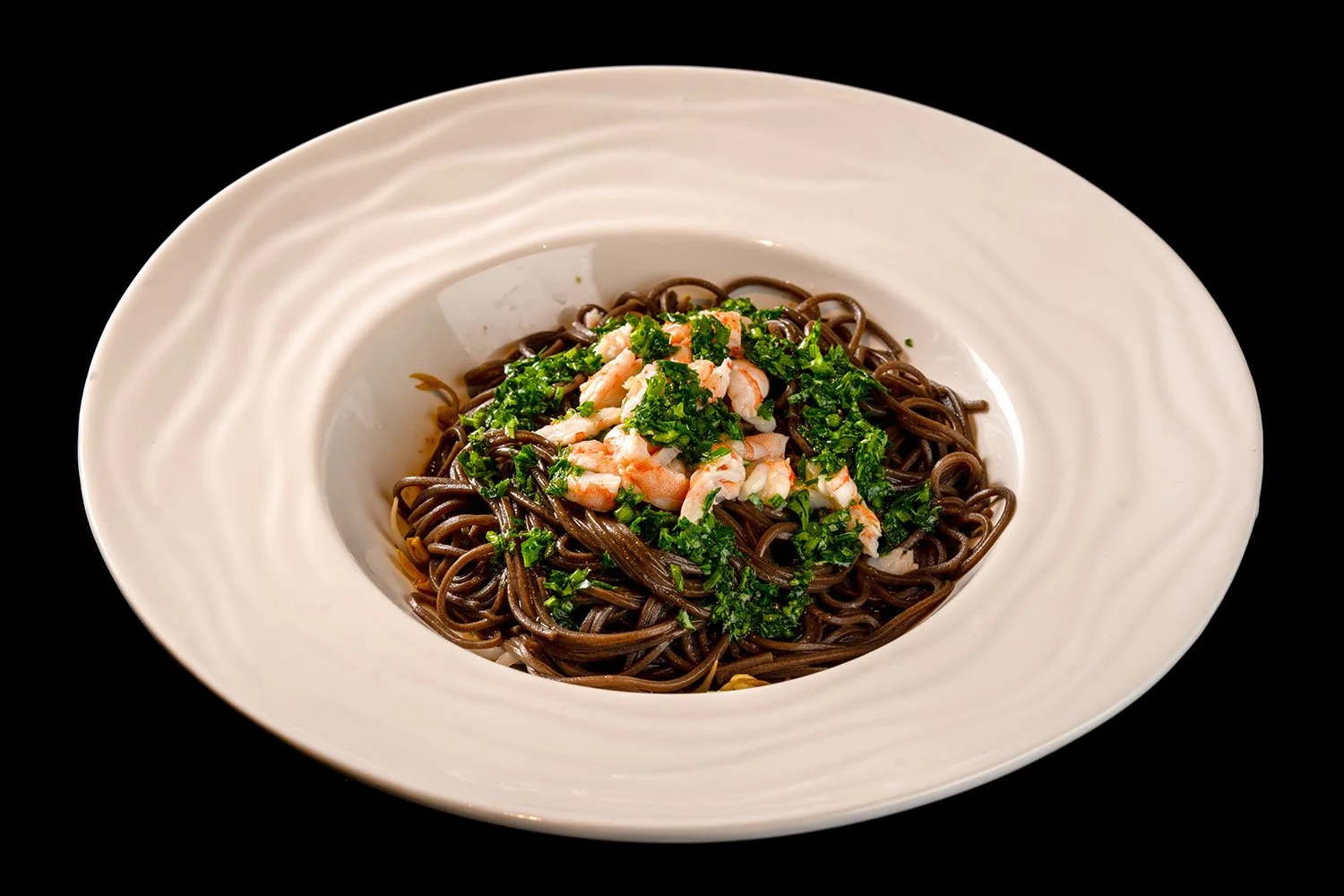 Schüssel mit dunklen Nudeln, Garnelen und gehackten grünen Kräutern auf schwarzem Hintergrund