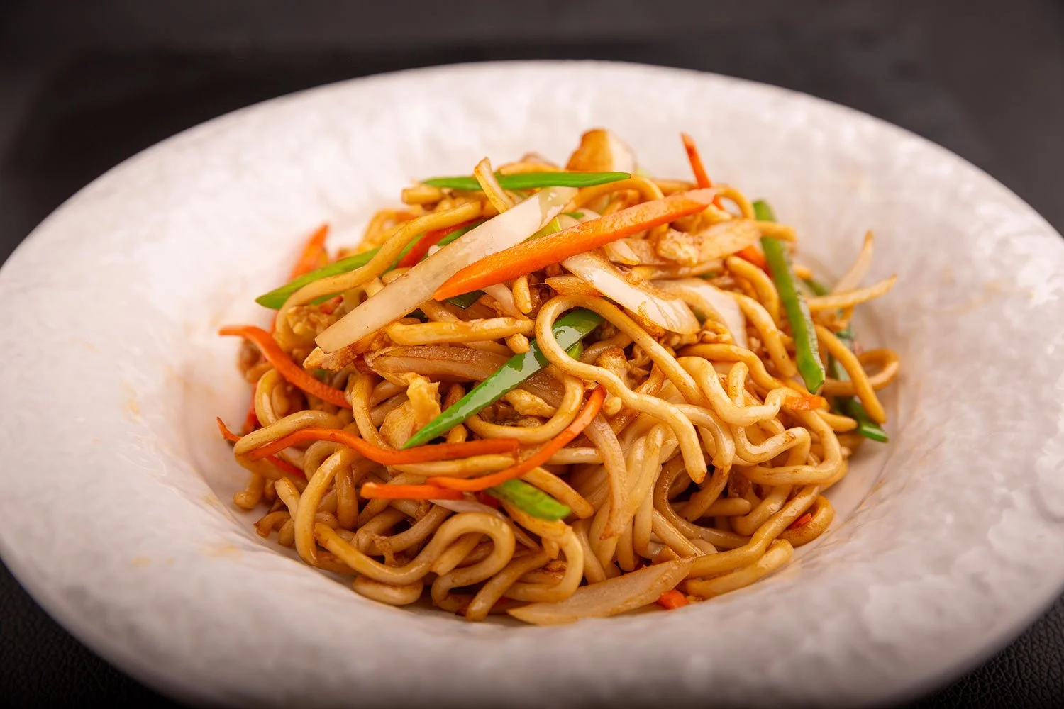 Schüssel mit gebratenen Nudeln und Gemüse, inklusive Karotten, Paprika und Zwiebeln.