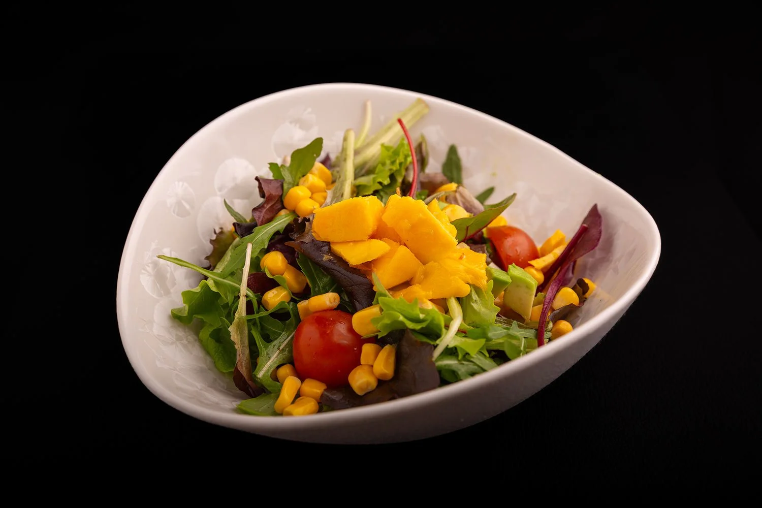 Frischer grüner Salat mit Tomaten, Mais und gewürfeltem Käse in einer weißen Schüssel.