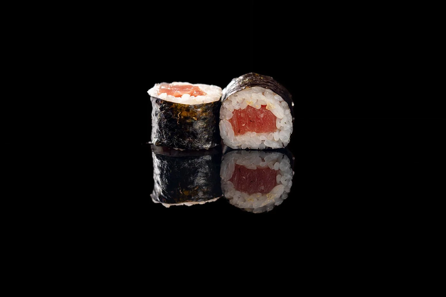 Zwei Sushi-Rollen mit rotem Fisch und algenblatt auf schwarzem Hintergrund, reflektiert auf der Oberfläche.