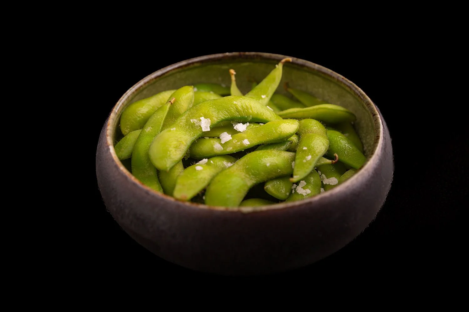 Grüner Edamame in einer dunklen Schüssel mit Salz