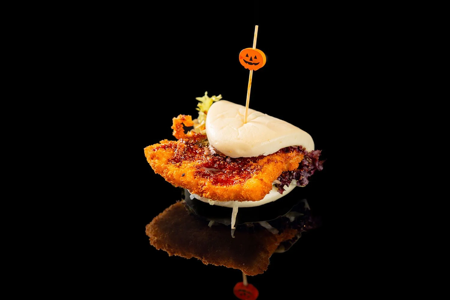 Mini-Hamburger mit paniertem Hähnchenstück, Salat, Ketchup, Petersilienblatt und Halloween-Kürbis-Spiestab auf schwarzem Hintergrund