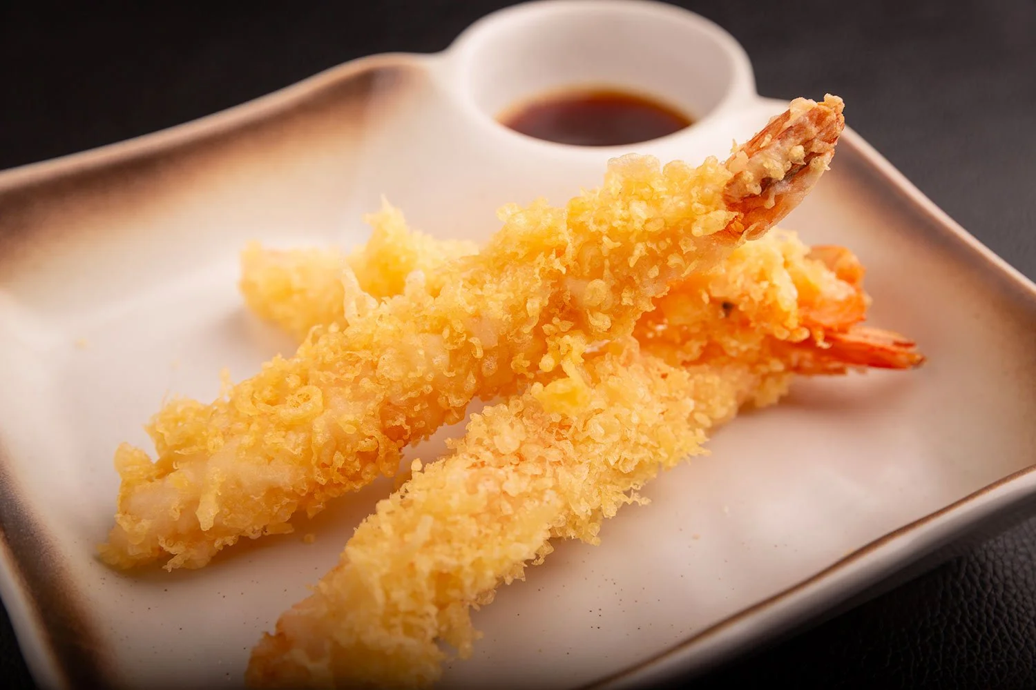 Zwei gebratene Garnelenspieße mit Dörrfisch auf einem weißen Teller, dazu Tsukemono-Sauce in einem kleinen Becher.