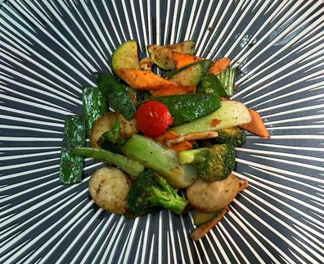 Restliche gegrillte Gemüse, einschließlich Zucchini, Karotten, Brokkoli, Pilze, Paprika und Tomaten, in einem schwarzen und weißen, streifenförmigen Teller.