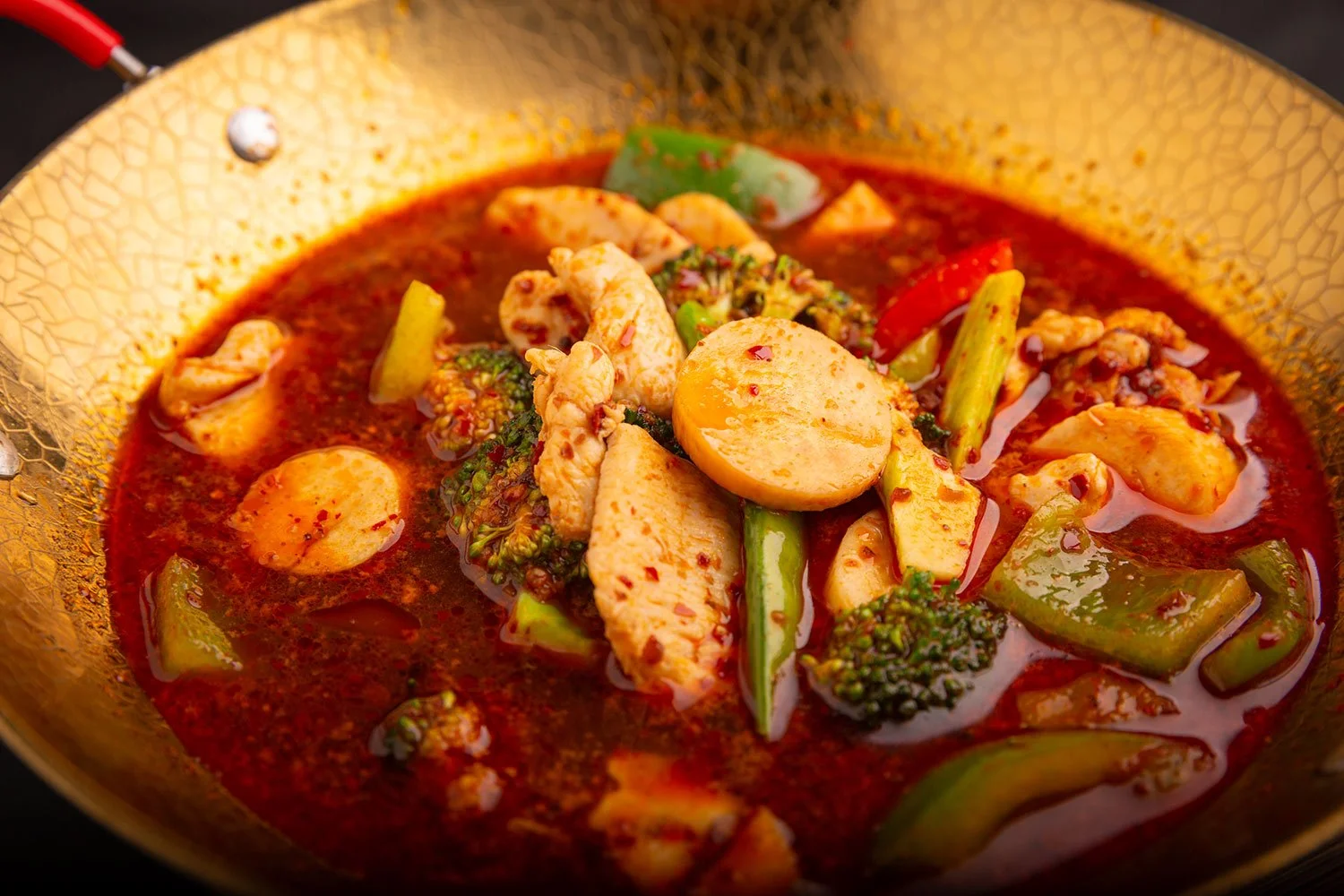 Hähnchen- und Brokkoligericht in einer goldenen Pfanne mit roter Sauce.