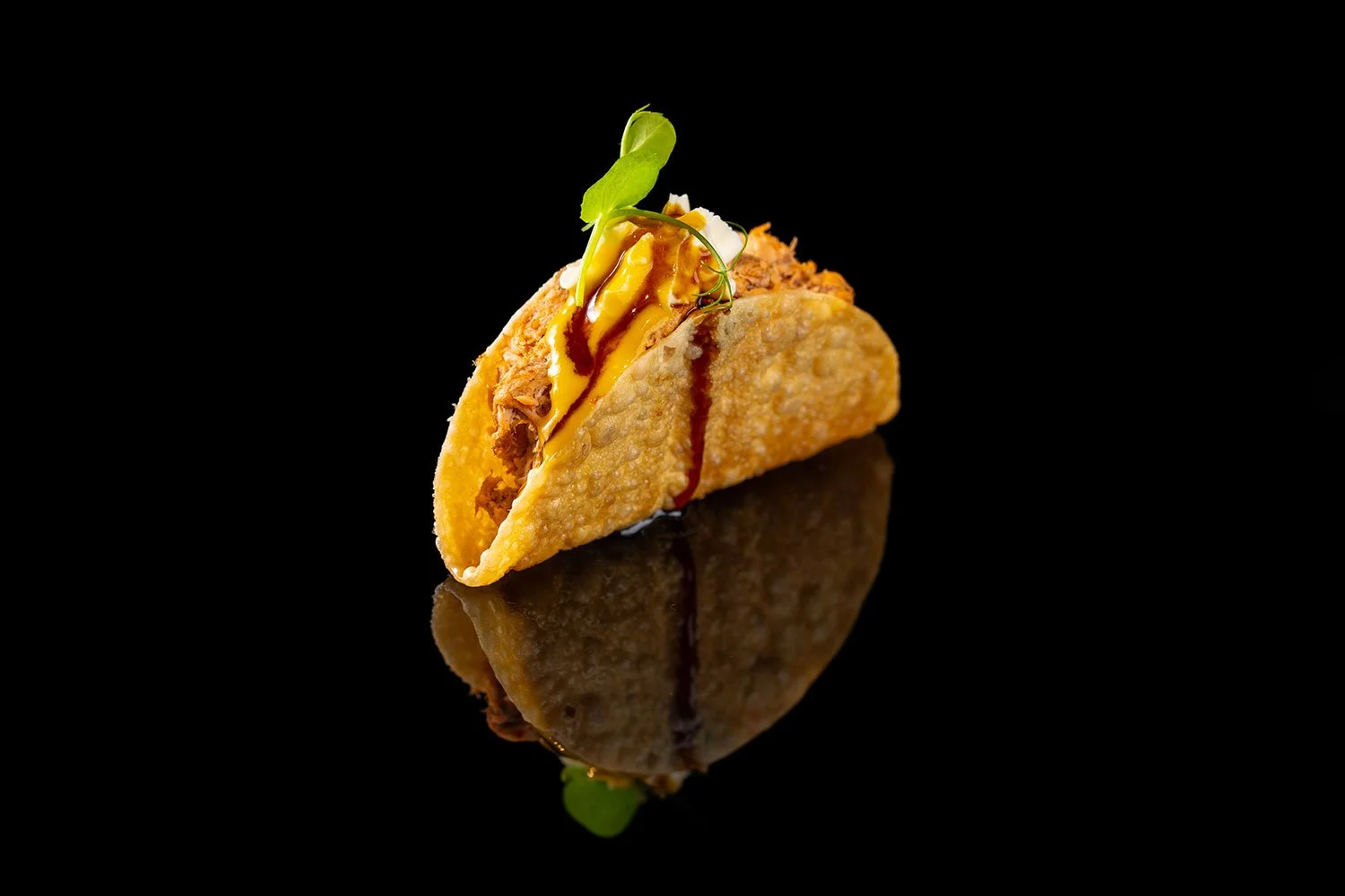 Fisch-Taco mit Salat, Sauce und Garnitur auf einem schwarzen Hintergrund, reflektierend.