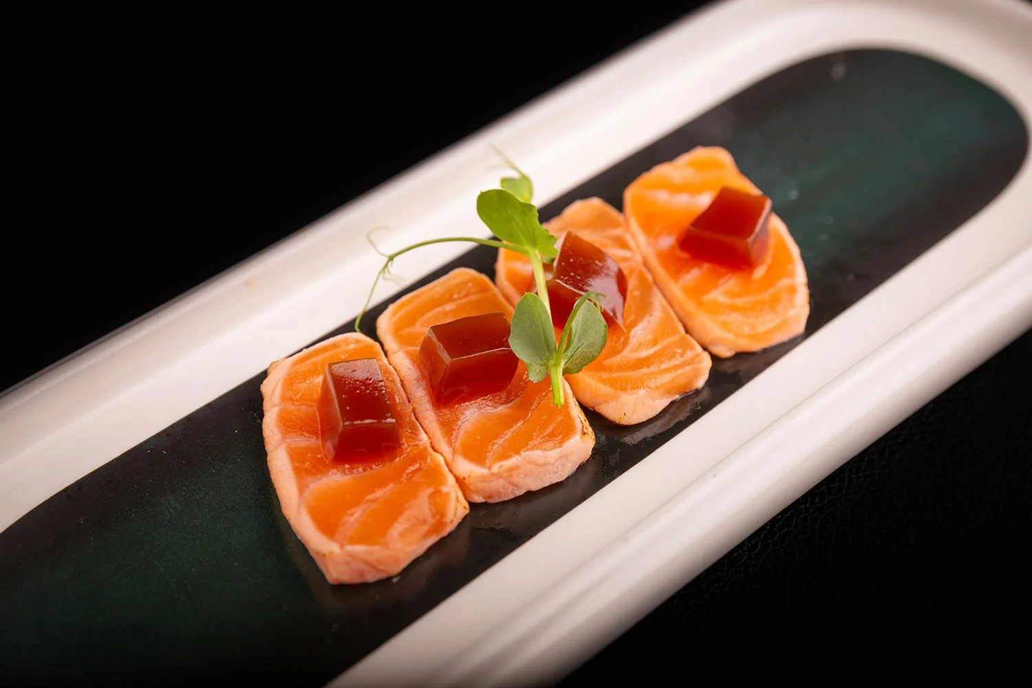 Lachs-Tatar mit roter Gelee und Kresse auf einem schwarzen und weißen Teller.