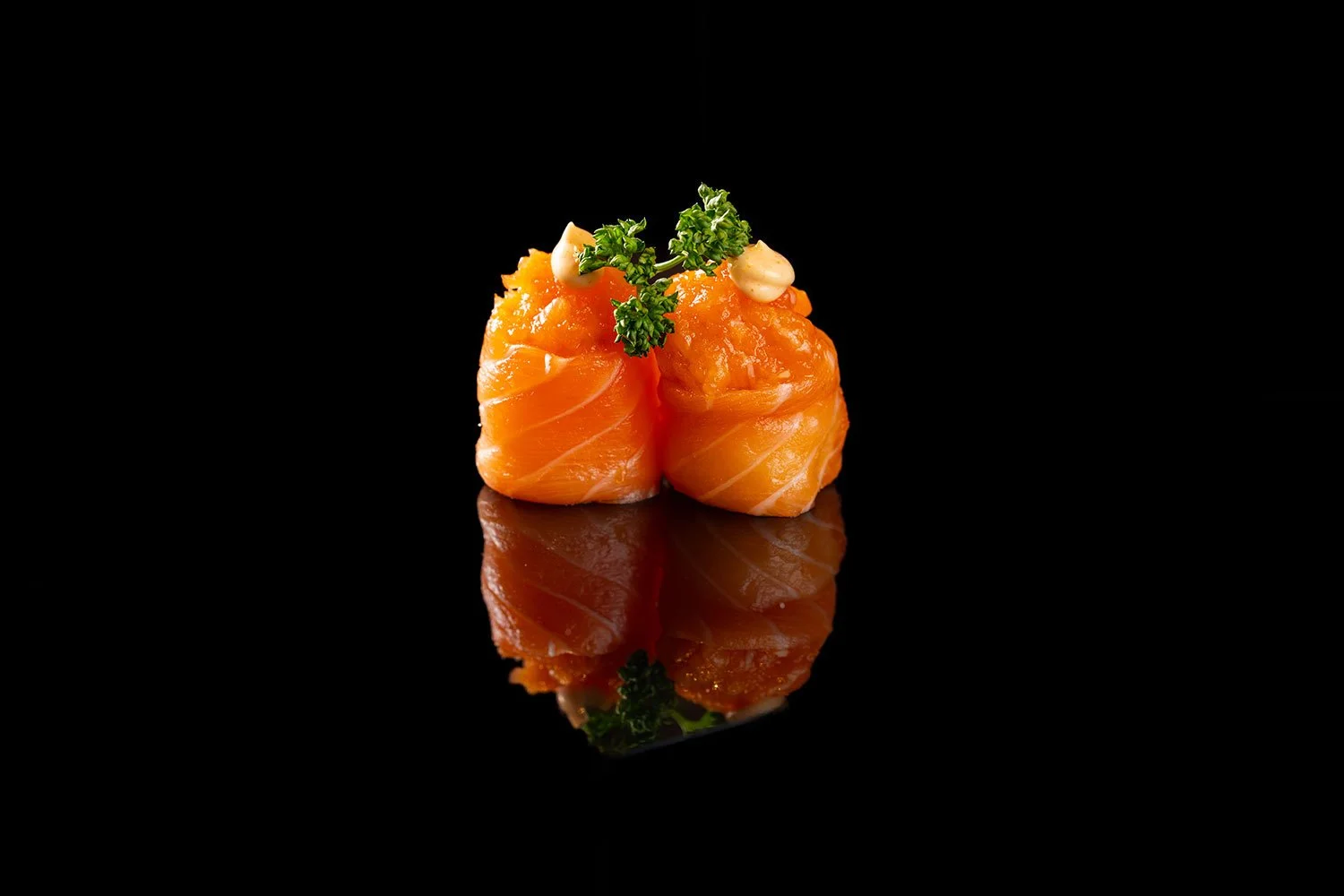 Zwei Lachs-Tataki mit Koriander und Mayonnaise auf schwarzem Hintergrund mit Reflexion.