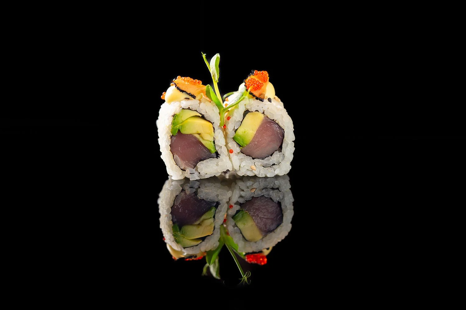 Sushi-Rolle mit Fisch, Avocado, Garnelen, großzügigem Fisch- und Avocadobezug, mit kleinen roten Fischrogen und grünen Kräutern auf schwarzem Hintergrund, mit Spiegelung