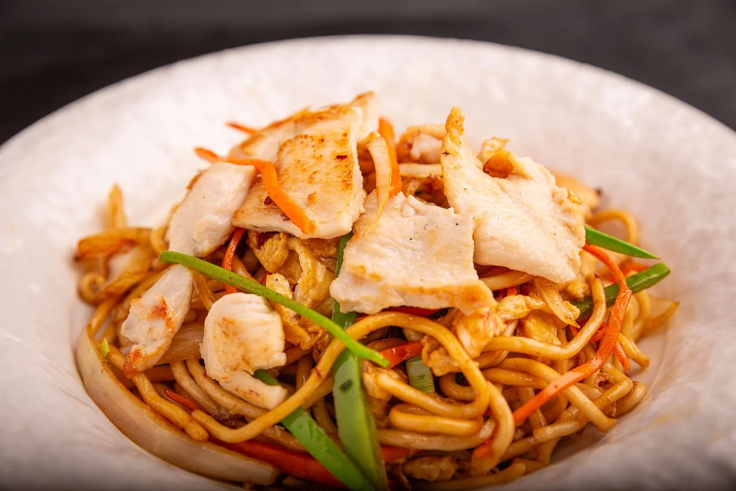 Nudeln mit Hähnchen, Gemüse und Sojasauce in einer weißen Schüssel.