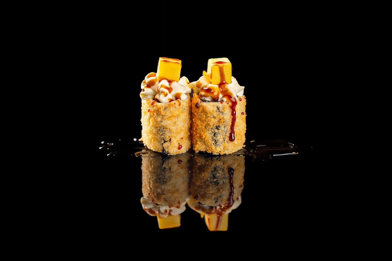 Zwei Sushi-Rollen mit Ente, mit Frischkäse, Sesam, Sojasauce, Mayonnaise und Mango, auf spiegelndem schwarzen Hintergrund