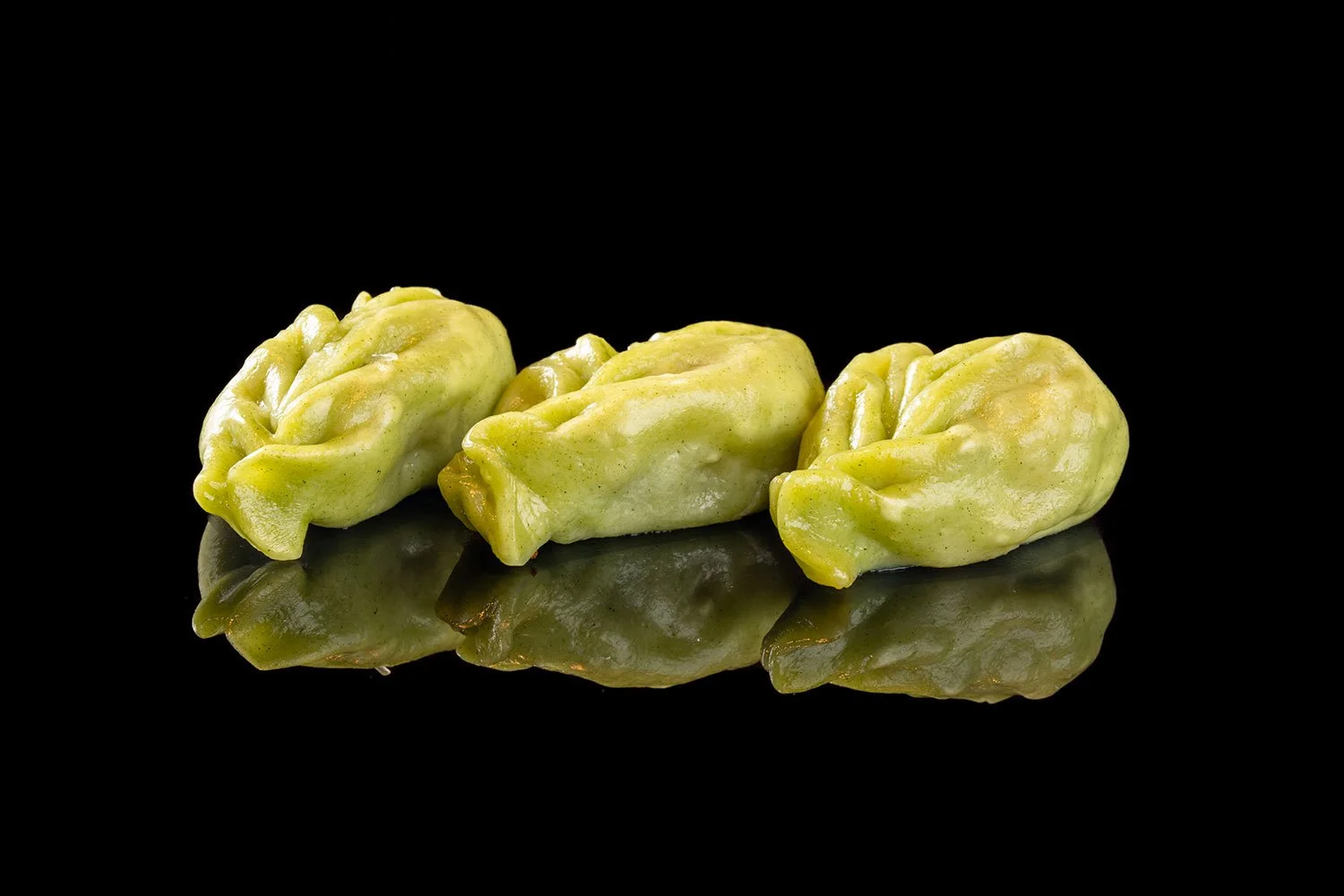 Drei grüne chinesische Teigtaschen auf schwarzem Spiegeluntergrund