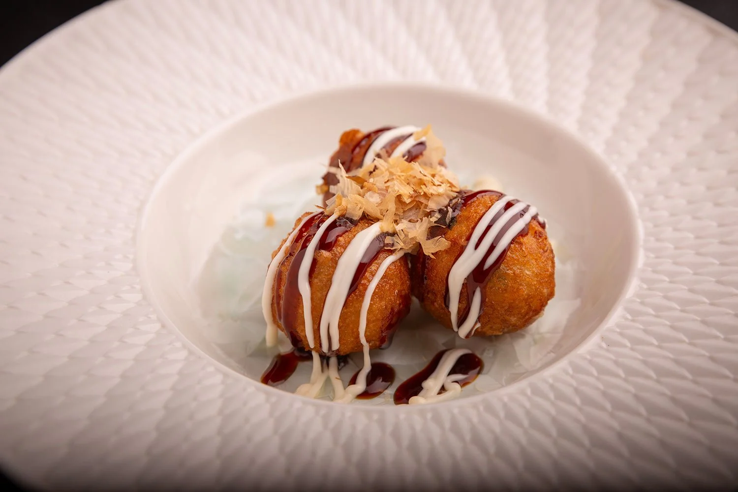 Frittierte Bällchen mit Schokoladen- und Vanillesoße, garniert mit Schokoladenspänen auf einem weißen Teller.
