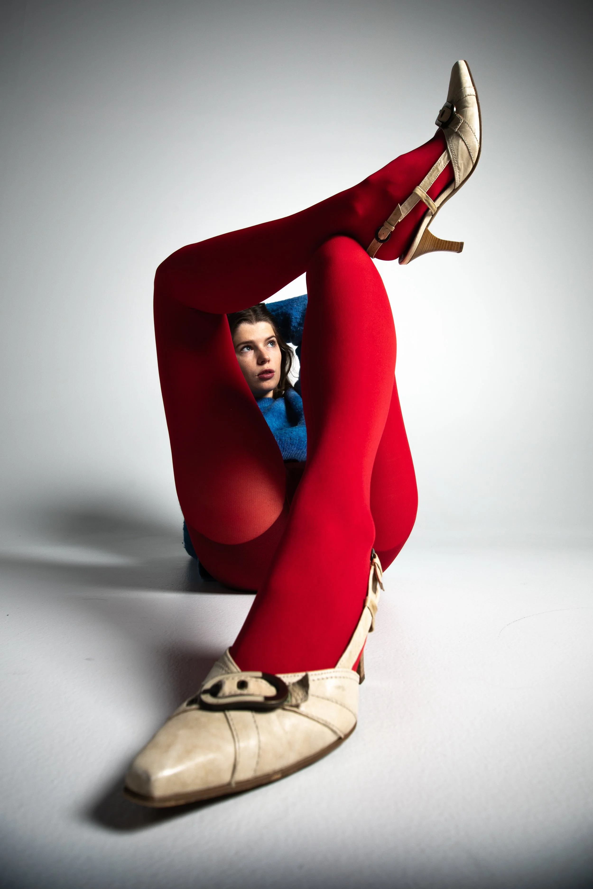 Füße in hohen beigen Schuhen mit roten Strümpfen, die hoch in die Luft gestreckt sind, auf weißem Hintergrund, Studiofotografie, Marie Becker