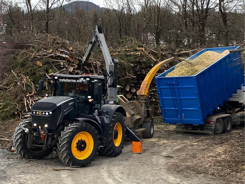 Veigående skogsmaskin med kran og en container med flis