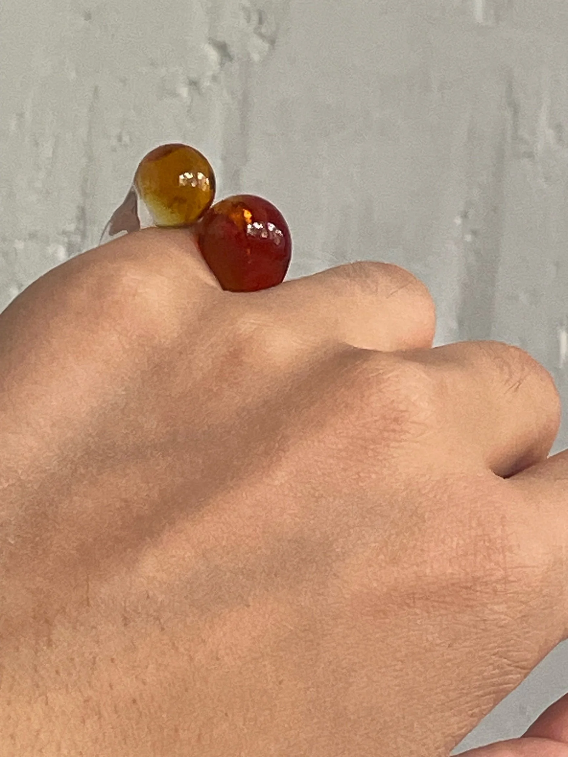 Anillo Blessed Eye Studio AMB Deco. Anillo en dedo meñique. Esferas de color ámbar. Fotografía con manos. Detalle