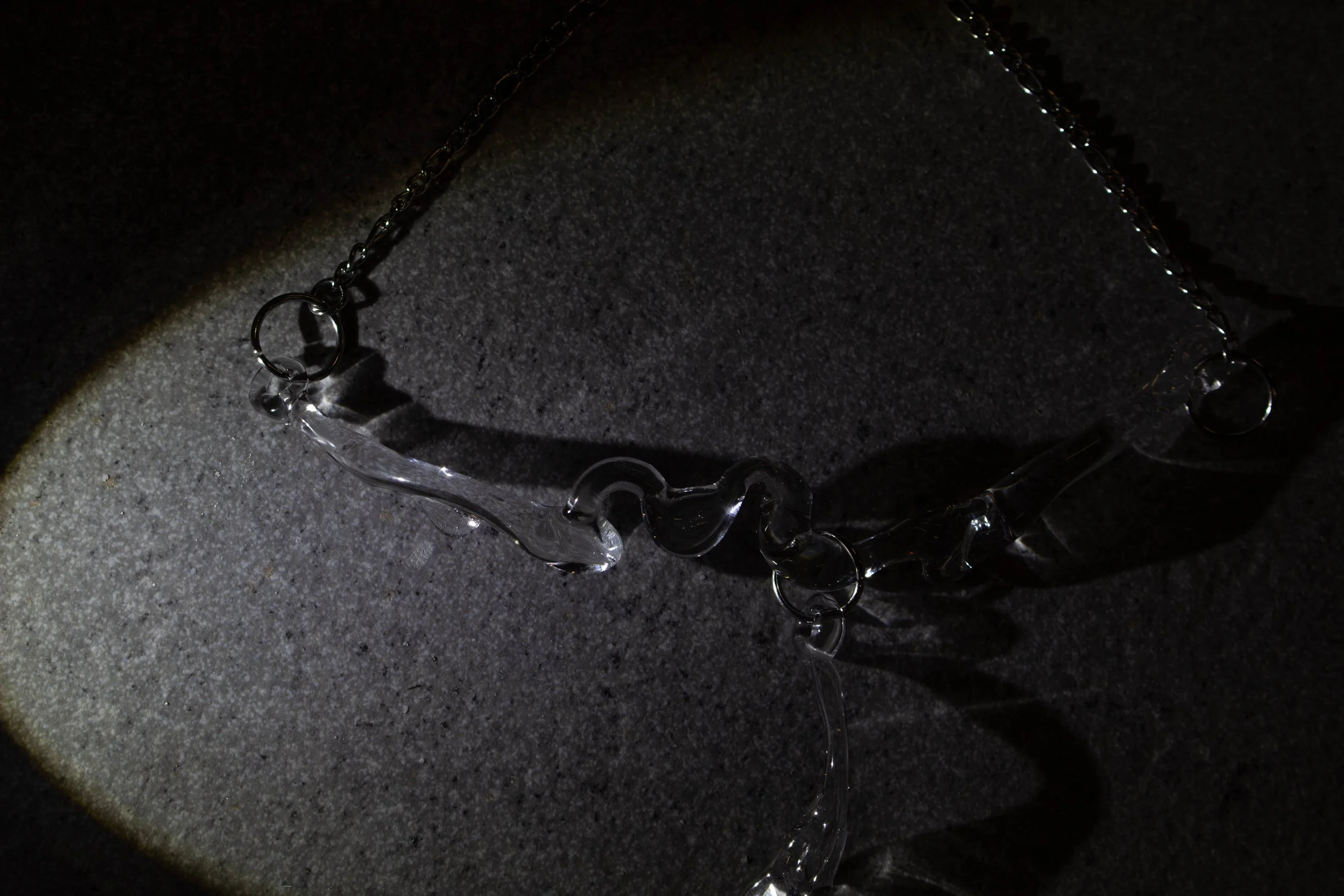 Collar de vidrio transparente con esferas y estructuras decorativas sobre una superficie gris oscura.