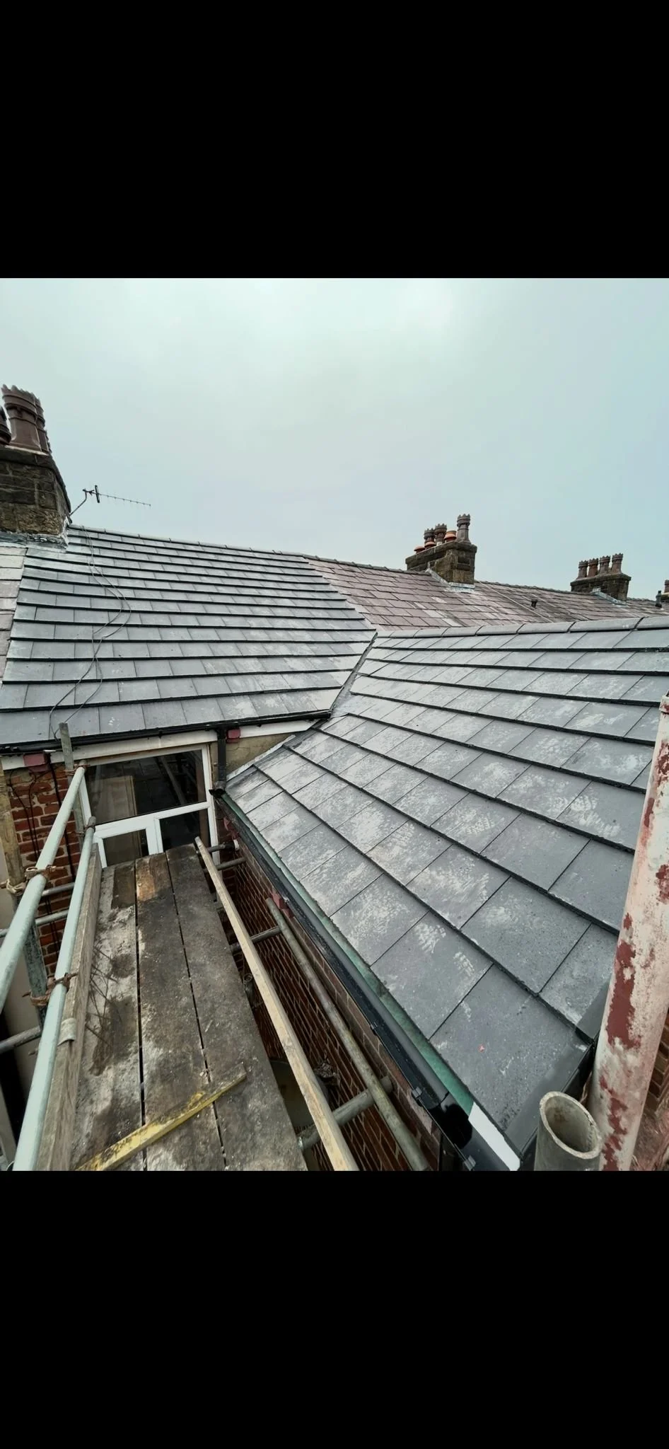 View of multiple rooftops with slate tiles and chimneys, taken from a scaffold on a building under renovation.