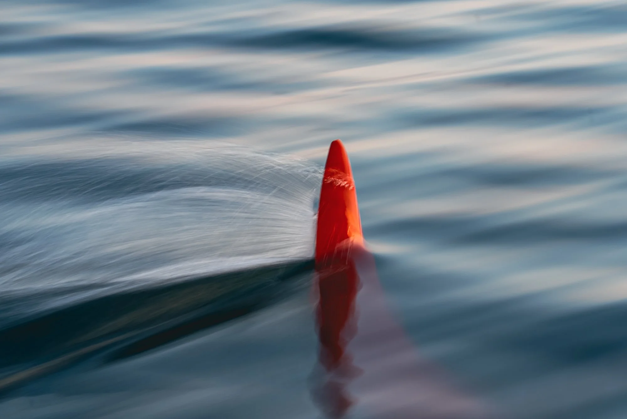 Close-up of a red buoy floating on the water with ripples and movement in the blue ocean.