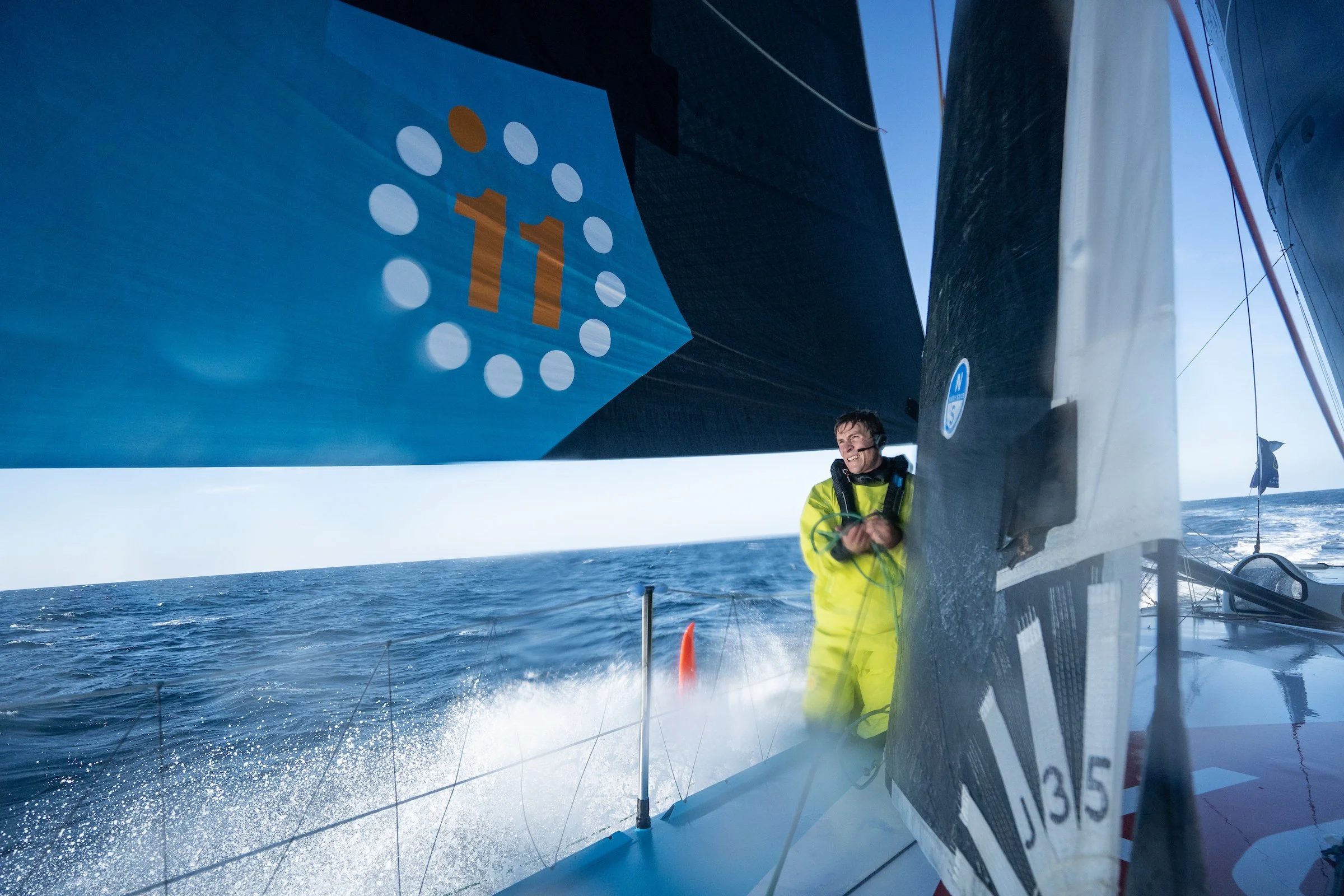 Sailor in yellow jacket smiling on a sailboat in open ocean with large sails