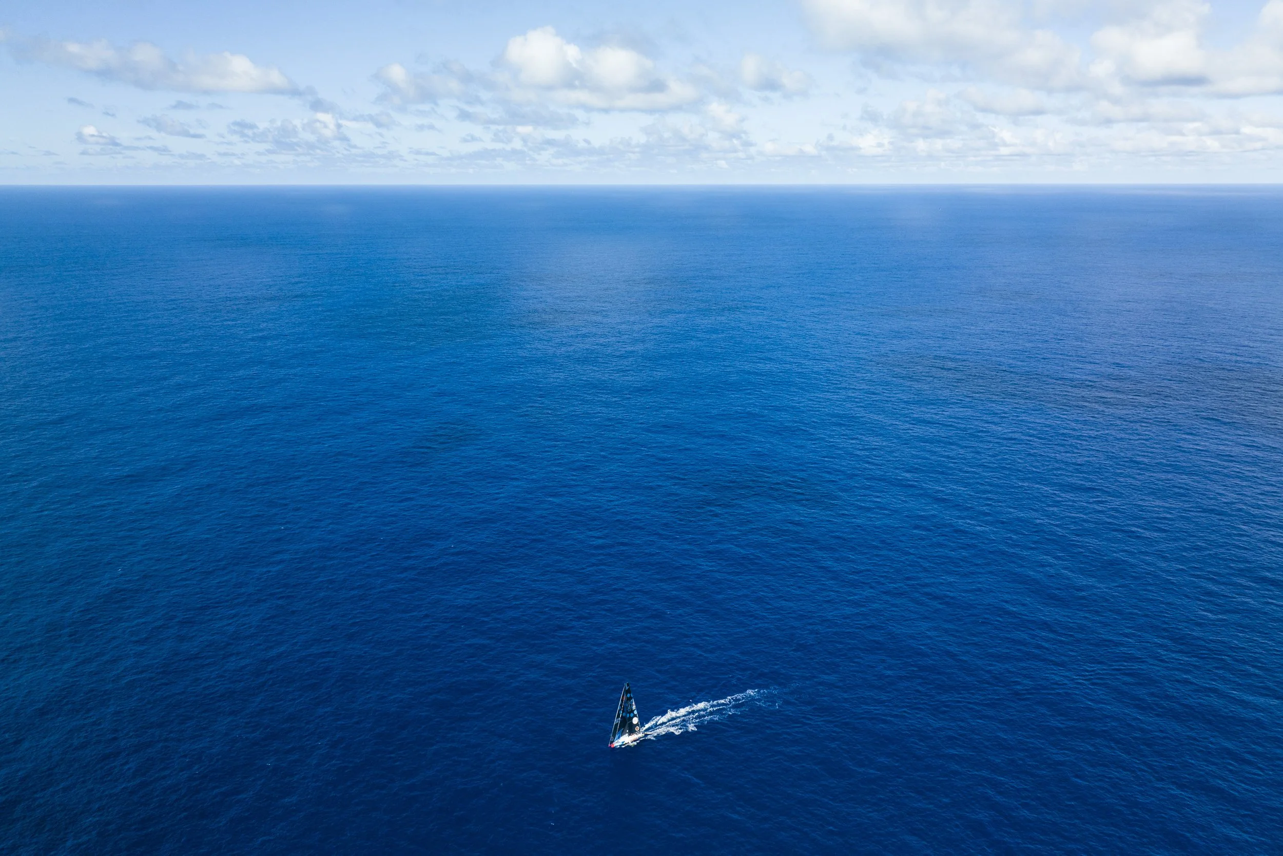 A sailboat sailing on a vast, deep blue ocean under a partly cloudy sky.