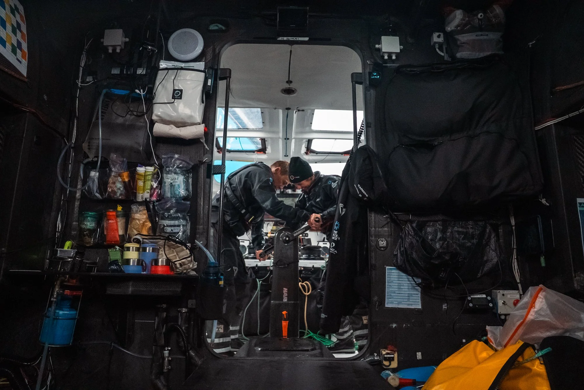 Two crew members working together inside the cockpit of a boat, organizing equipment and supplies.