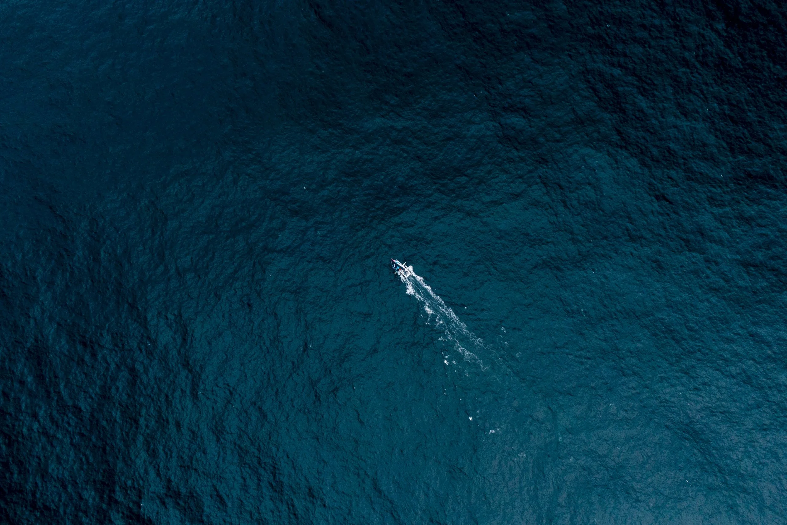 A small boat moving across the open ocean, leaving a trail of white wake behind it.