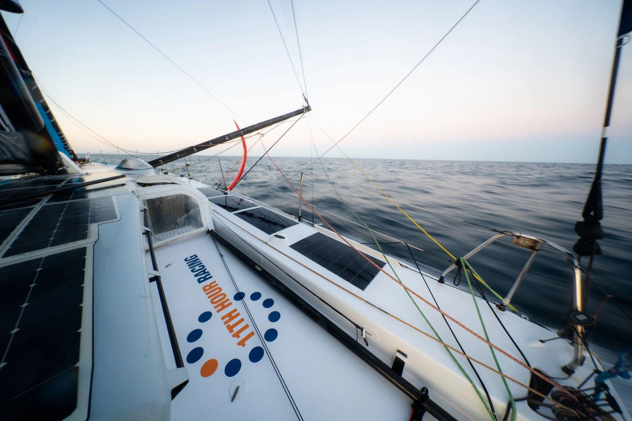 View from a sailing yacht with solar panels on deck, sailing on open water during sunset or sunrise.