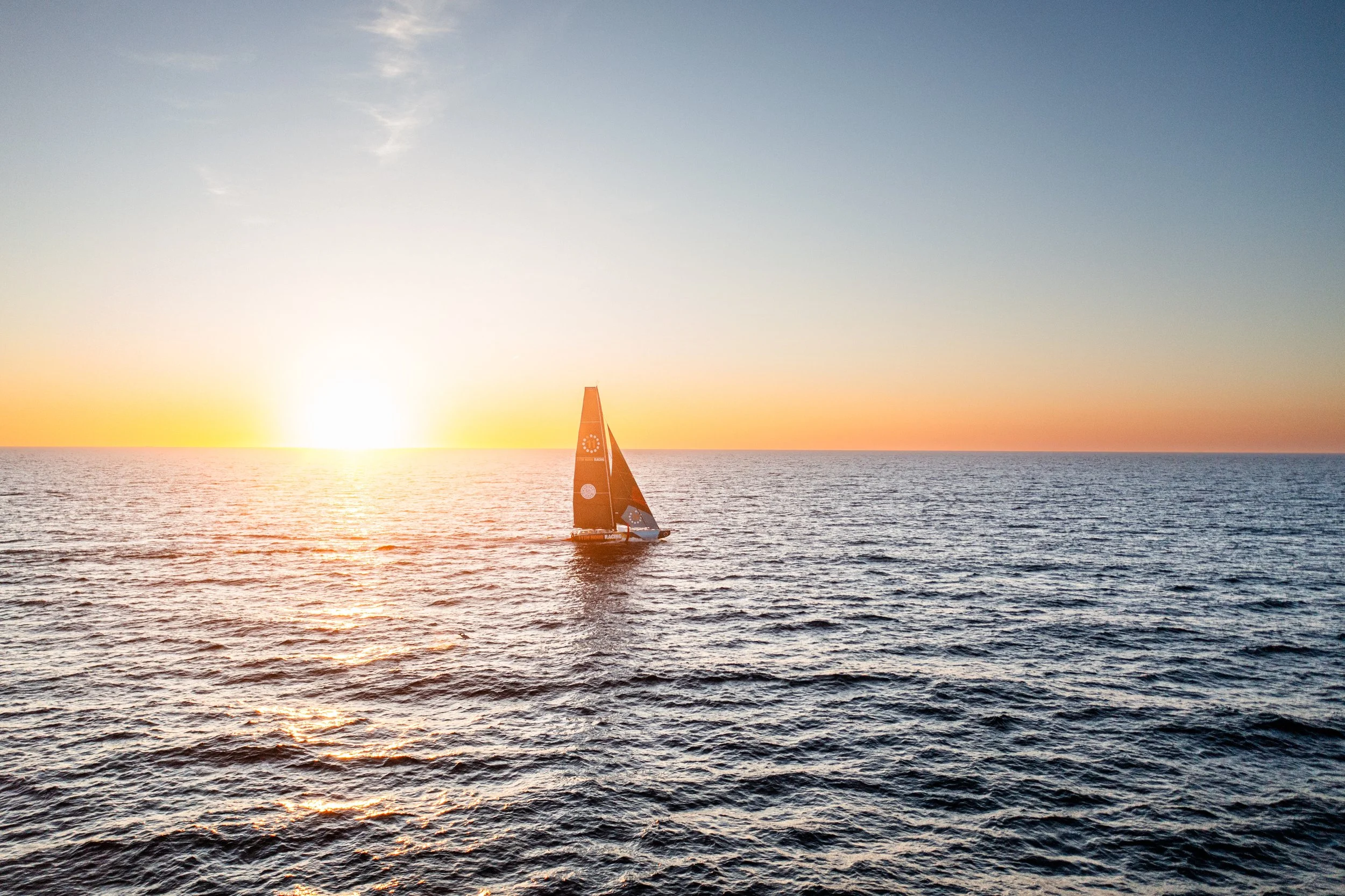 A sailboat sailing on the ocean during sunset with a clear sky.