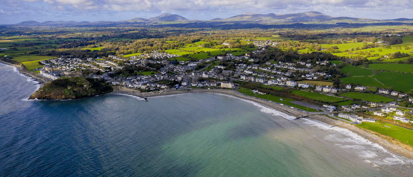 Aerial view of a coastal town with a beach, green fields, and rolling hills in the background.
