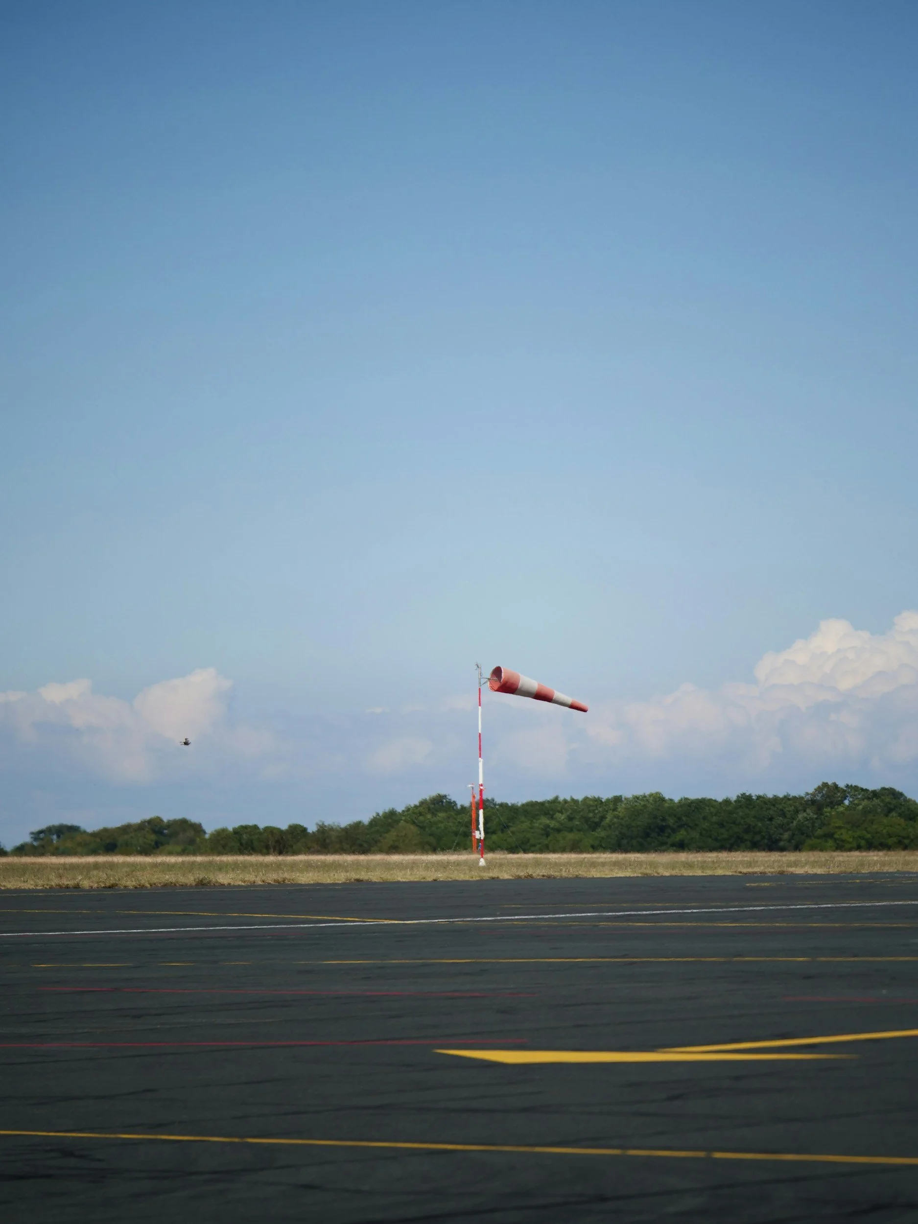 Ein Windstoß auf einem Flugplatz mit einem rot-weißen Windpark, im Hintergrund Bäume und ein blauer Himmel mit Wolken.