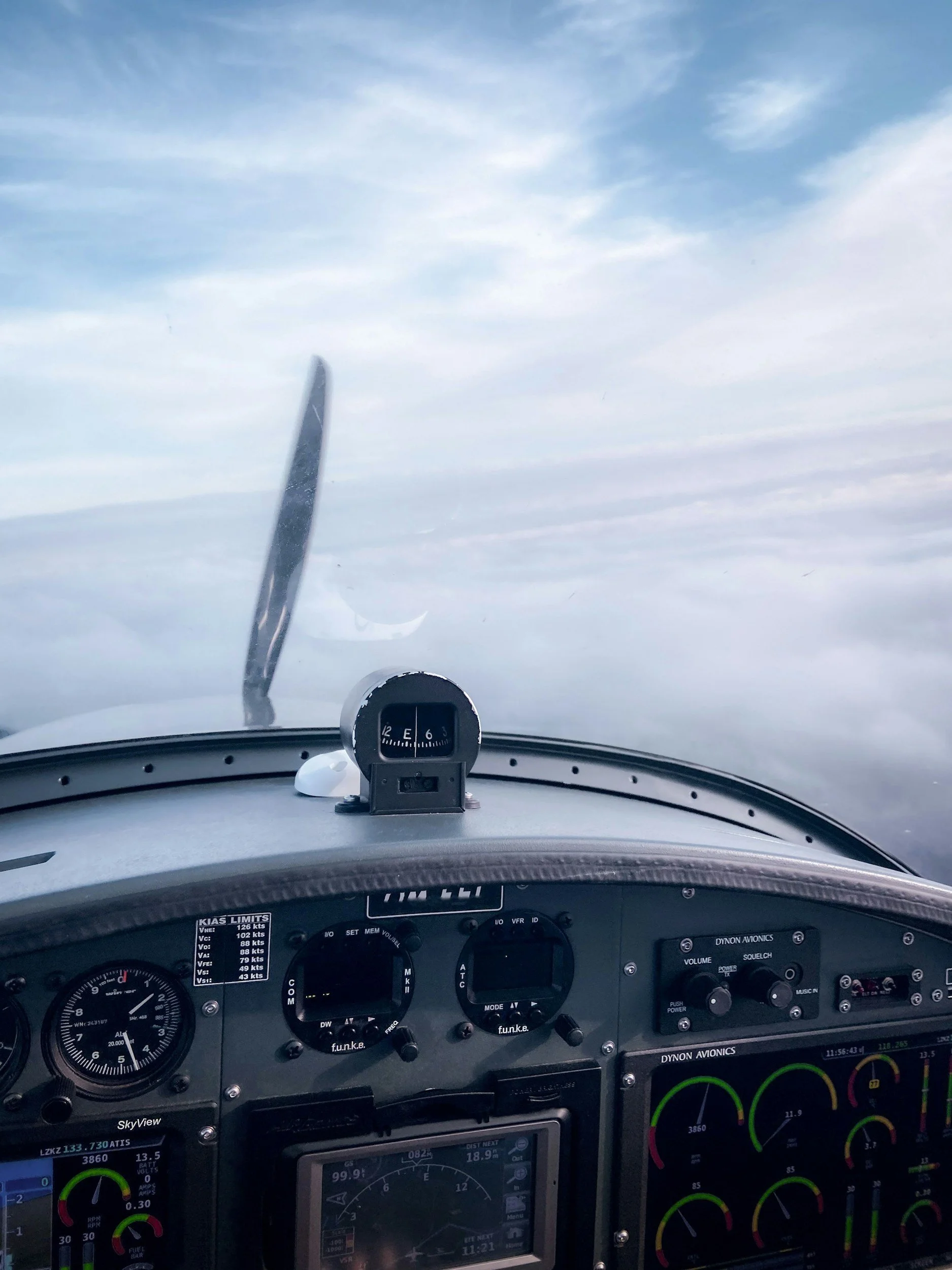 Cockpit eines Flugzeugs mit Instrumenten und Anzeige, Blick nach vorne auf den Himmel mit Wolken.