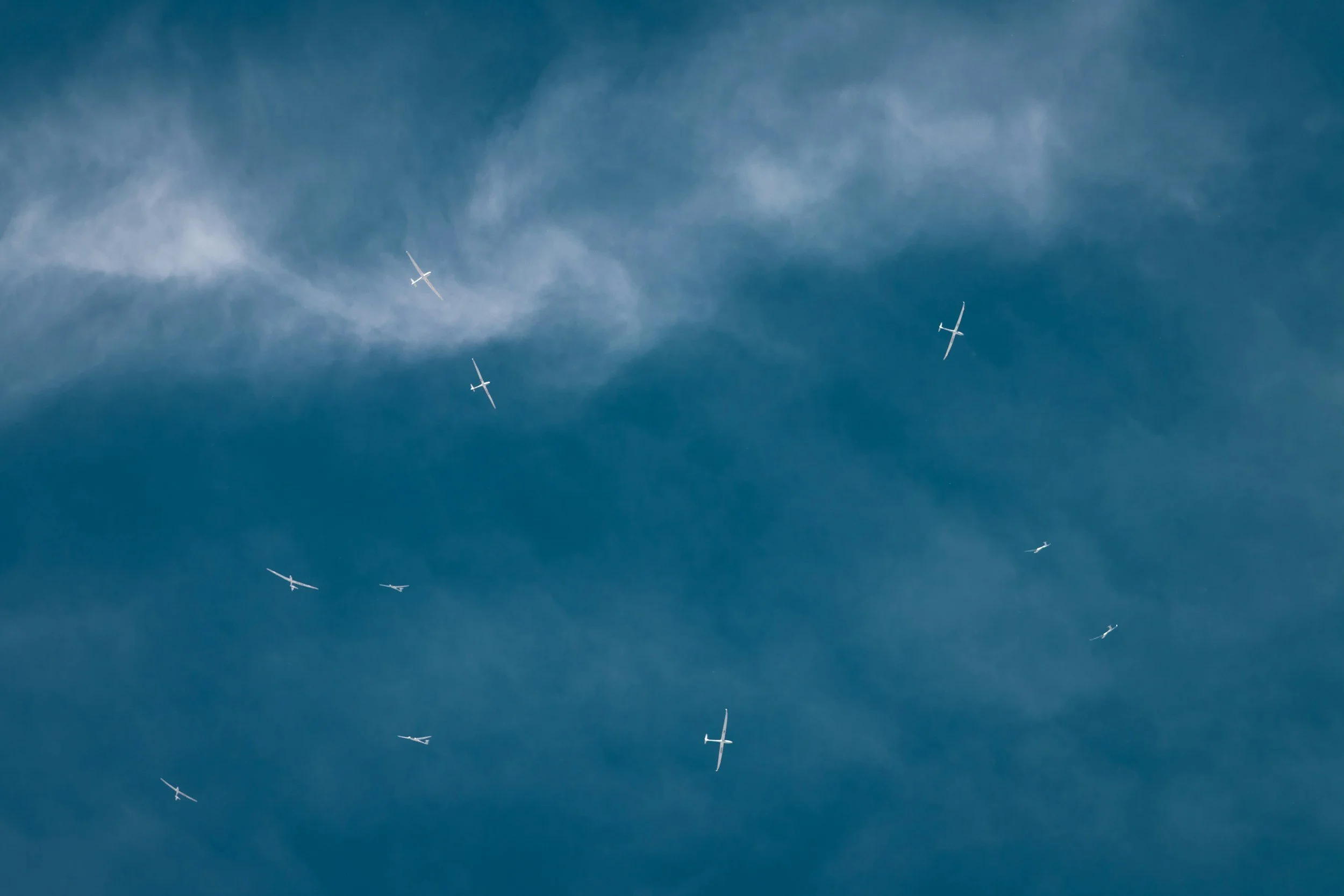 Mehrere Segelflugzeuge fliegen in formation durch den blauen Himmel mit dünnen Wolken.