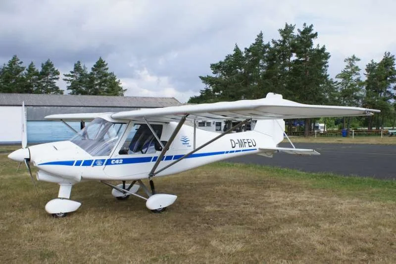Leichtflugzeug auf einer Landebahn mit Bäumen im Hintergrund