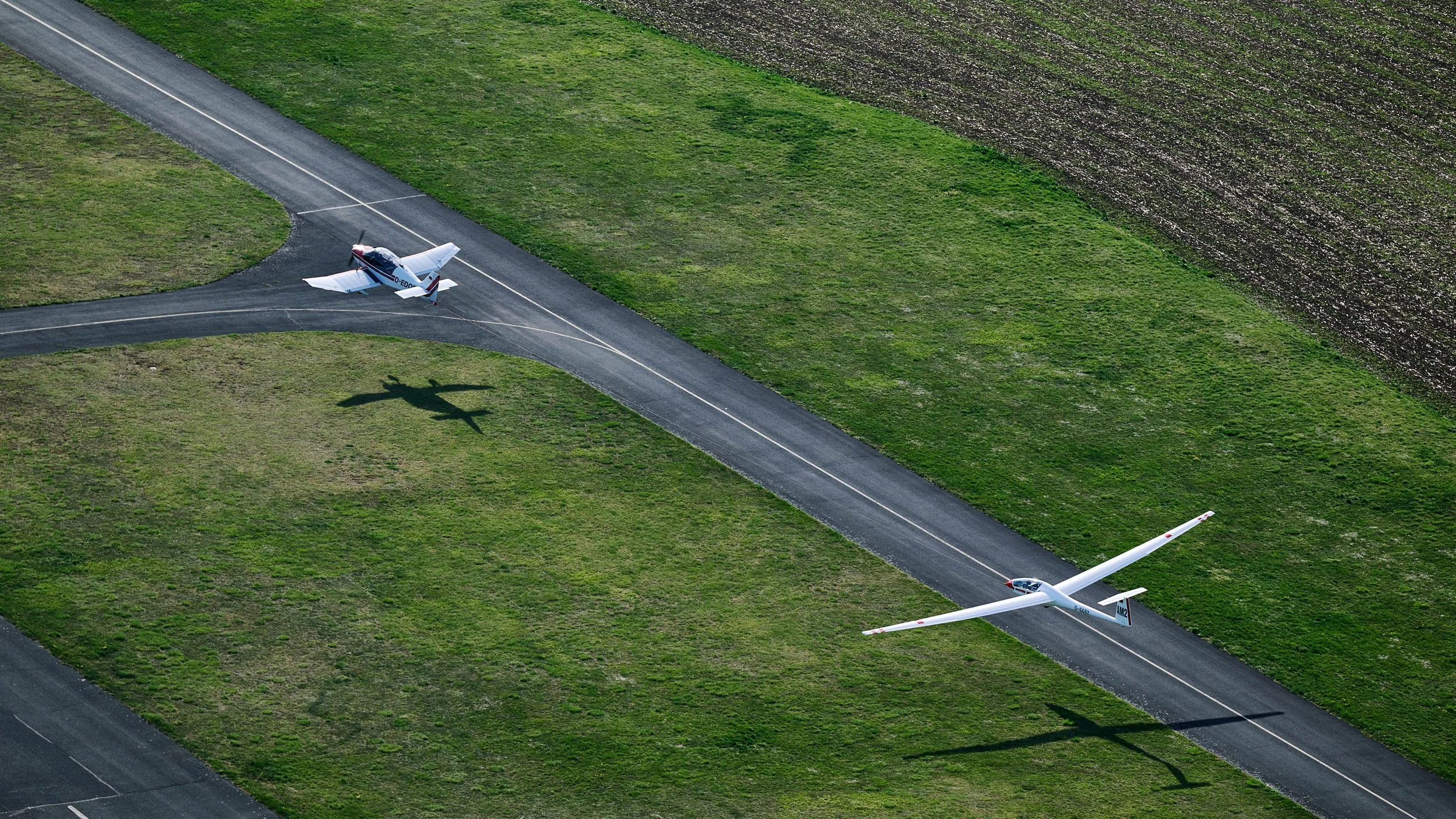 Zwei Segelflugzeuge im Flug über einer grünen Wiese, eine Szene aus der Luftaufnahme.