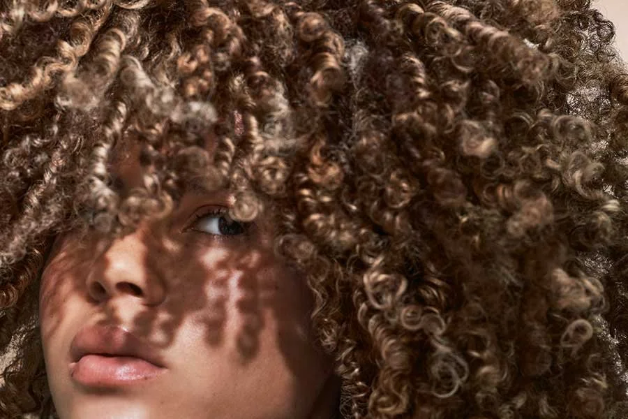 Close-up of a woman's face partially covered by voluminous, curly hair with shadows cast on her face.