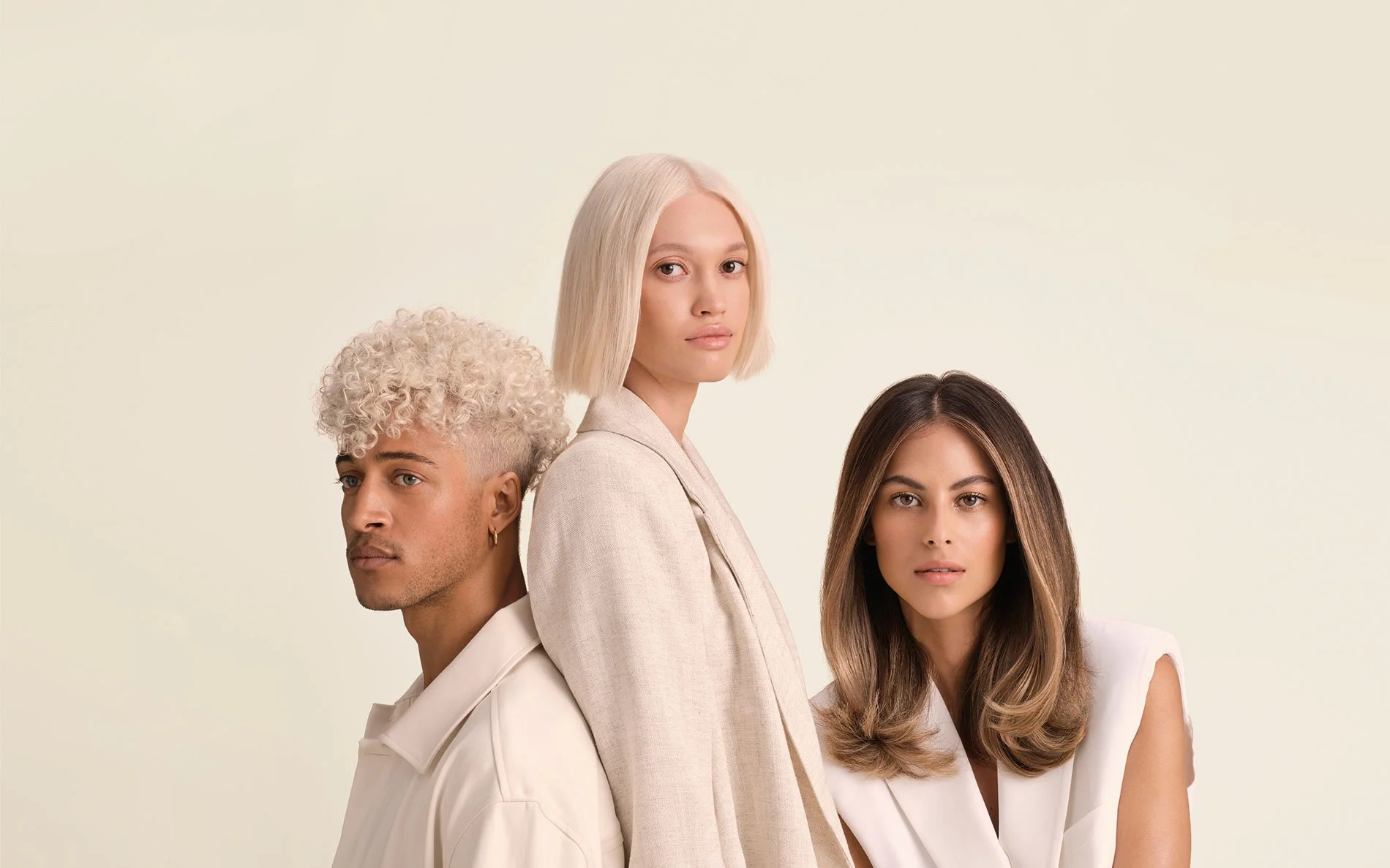 Three women with different hair colors and styles standing close together against a plain, light-colored background.