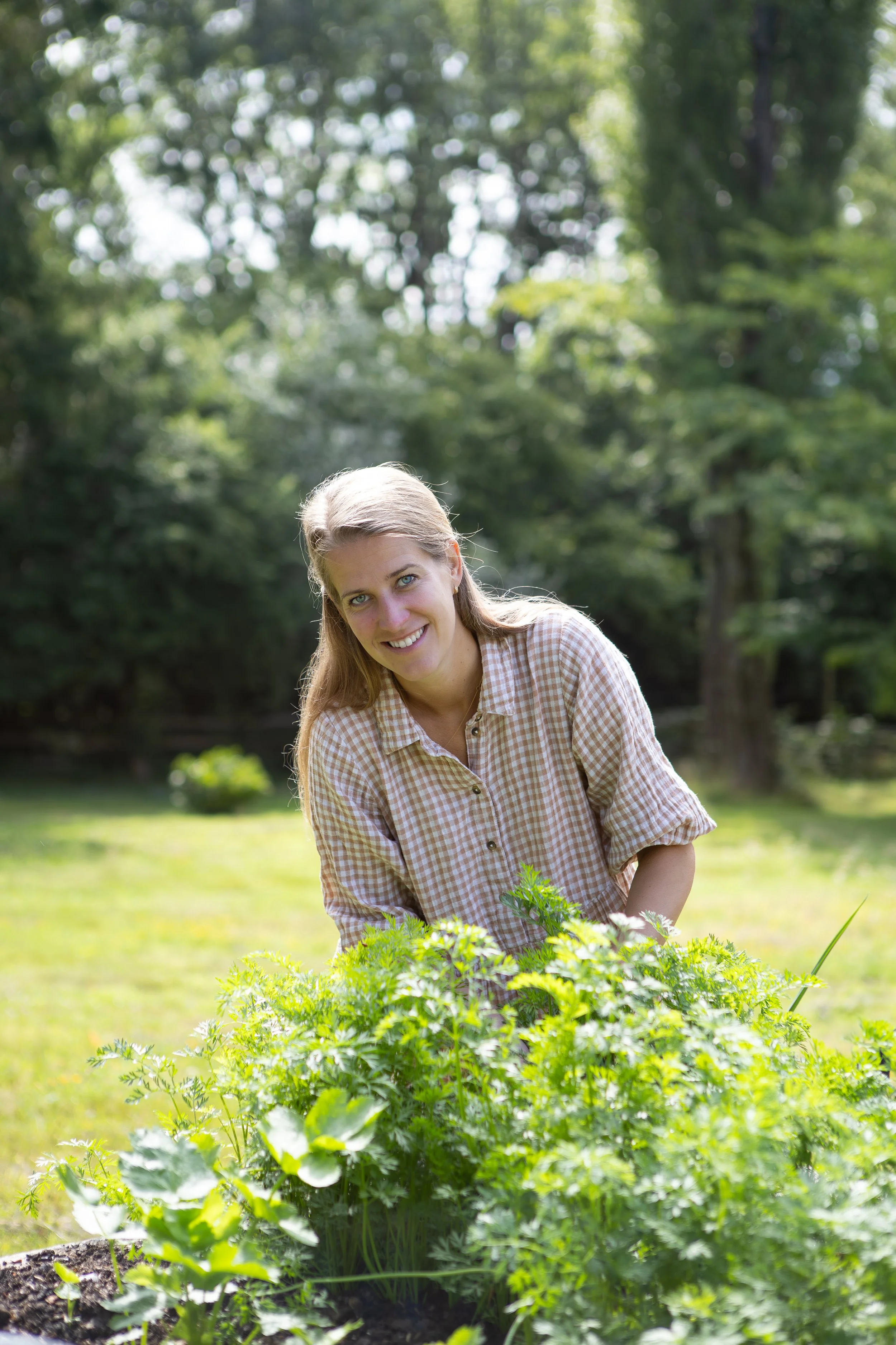 A woman with blonde hair and blue eyes tending to plants outdoors in a garden during the daytime