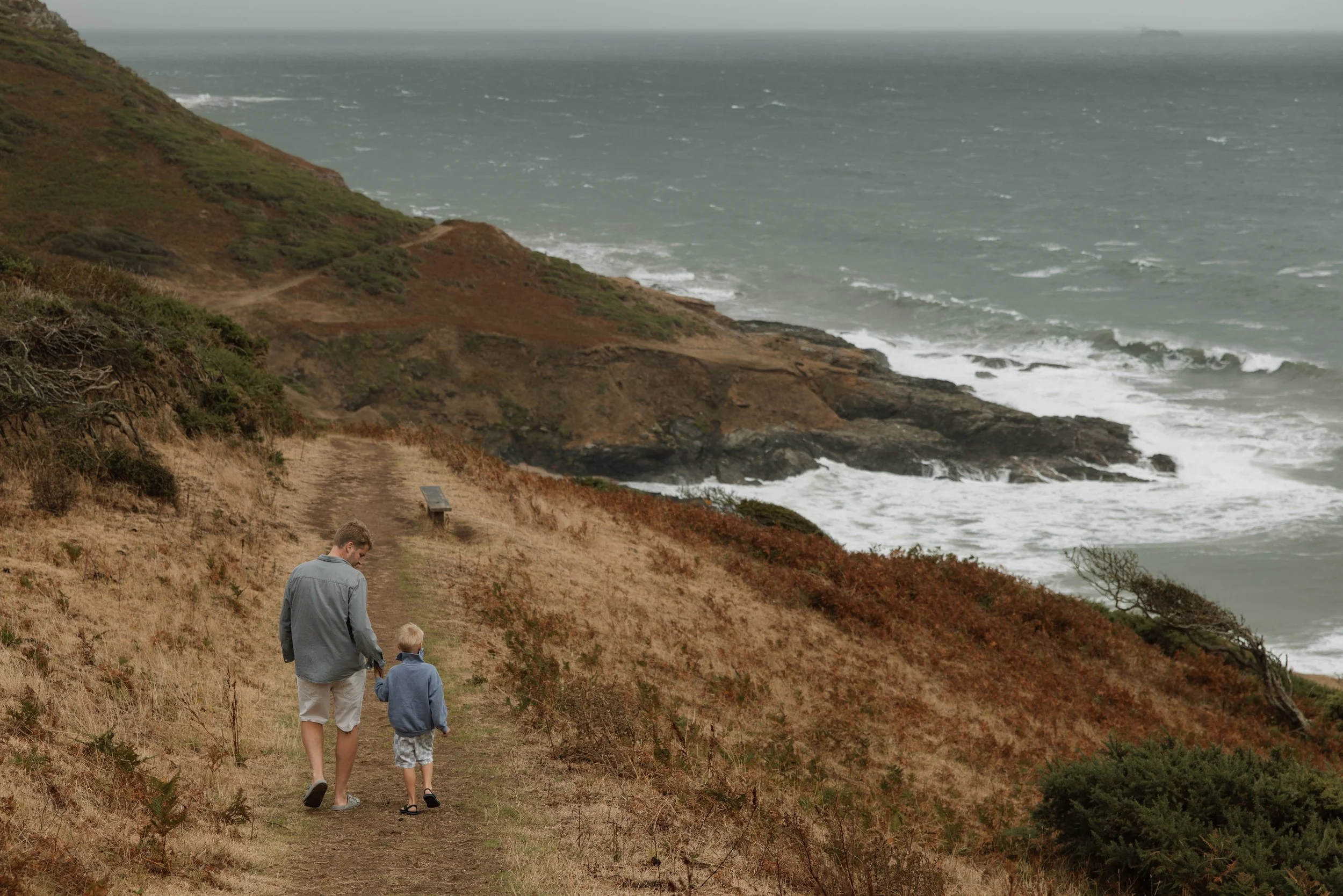 Children playing on a sandy beach with ocean waves and a distant coastline under a clear sky.