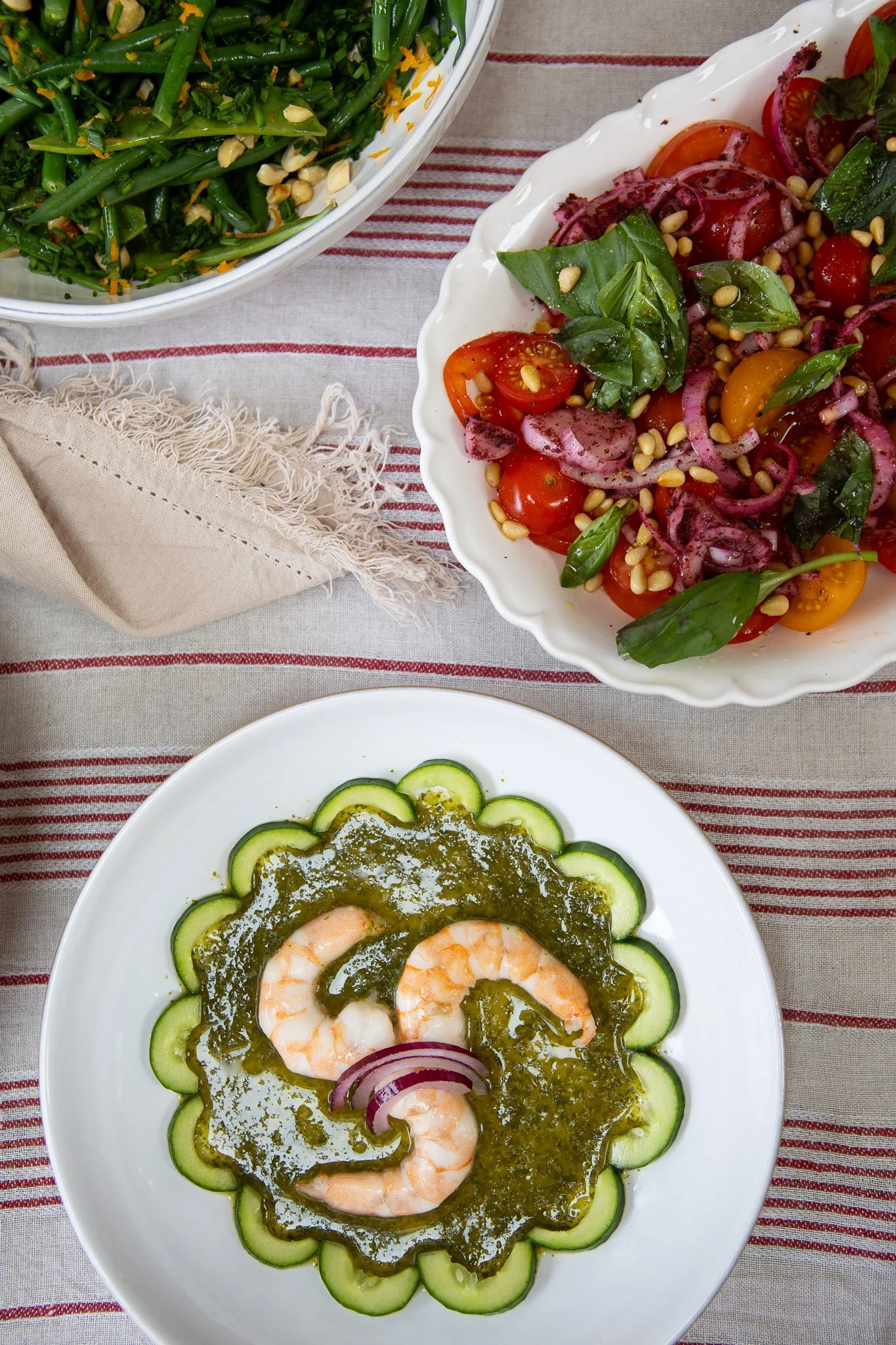 A white plate with shrimp and cucumber slices, topped with green sauce and garnished with red onion slices.