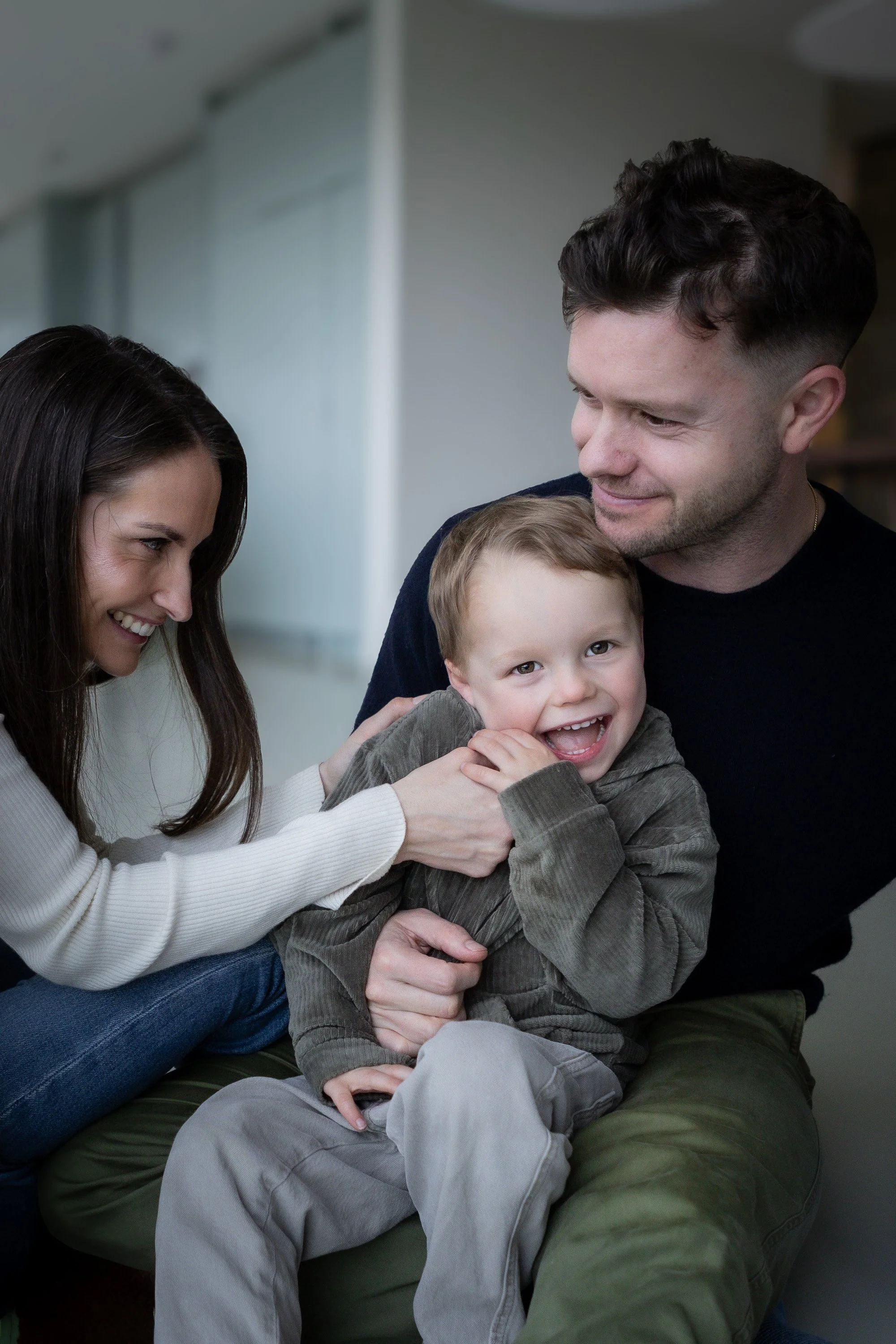 A family of three people, a woman, a man, and a young boy, sitting together on a couch in a living room, smiling and enjoying each other's company.